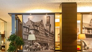 Eine Lobby mit einer Couch, Stühlen, einer Lampe, einem Blumentopf und einem großen gerahmten Bild von einem Gebäude.