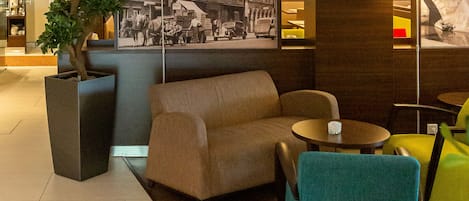 A lobby with a sofa, chairs, a lamp, a potted plant, and a large framed picture of a building.