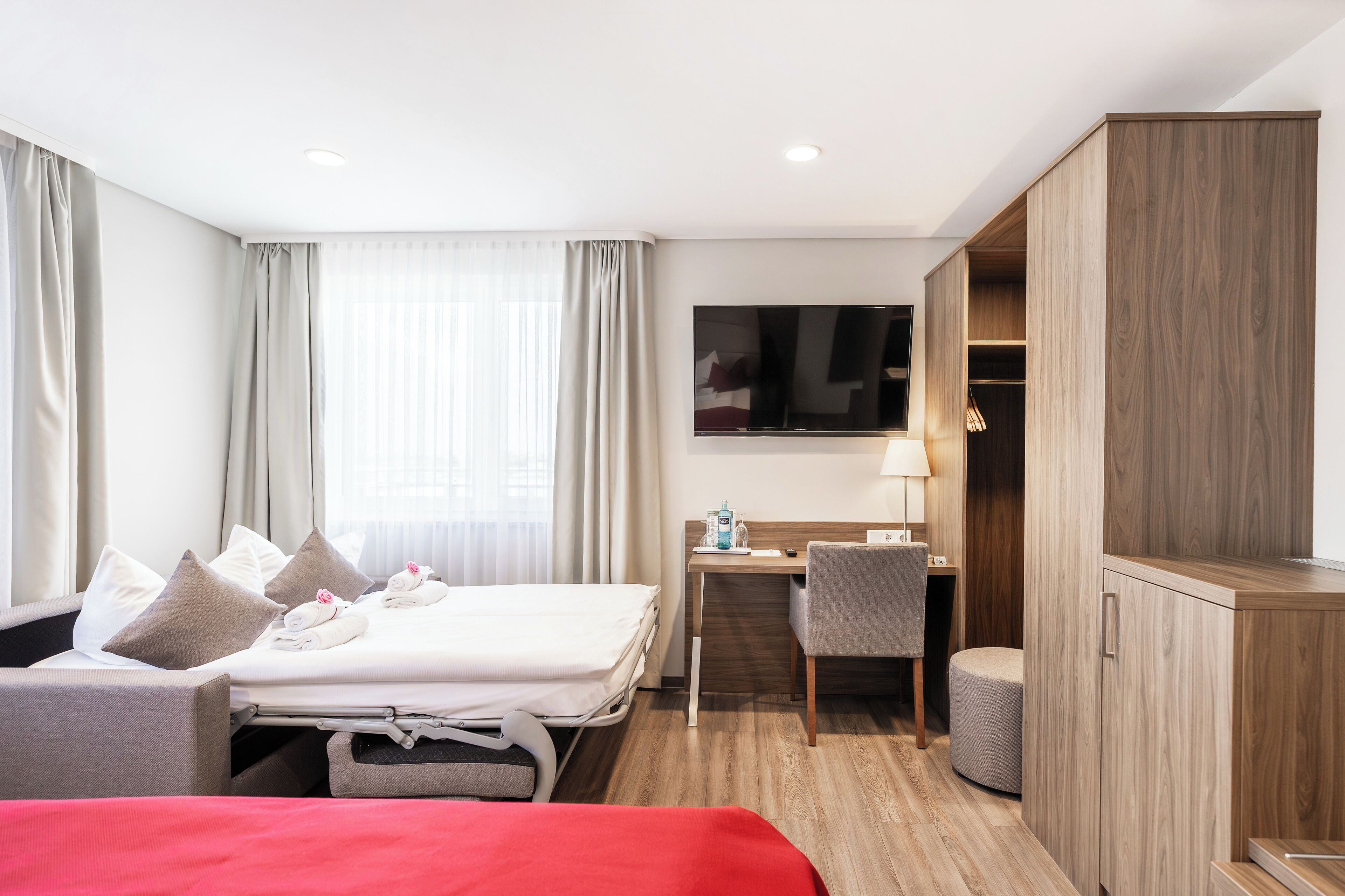Una habitación de hotel con cama, escritorio, silla, televisor y armario.