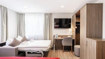 Una habitación de hotel con cama, escritorio, silla, televisor y armario.