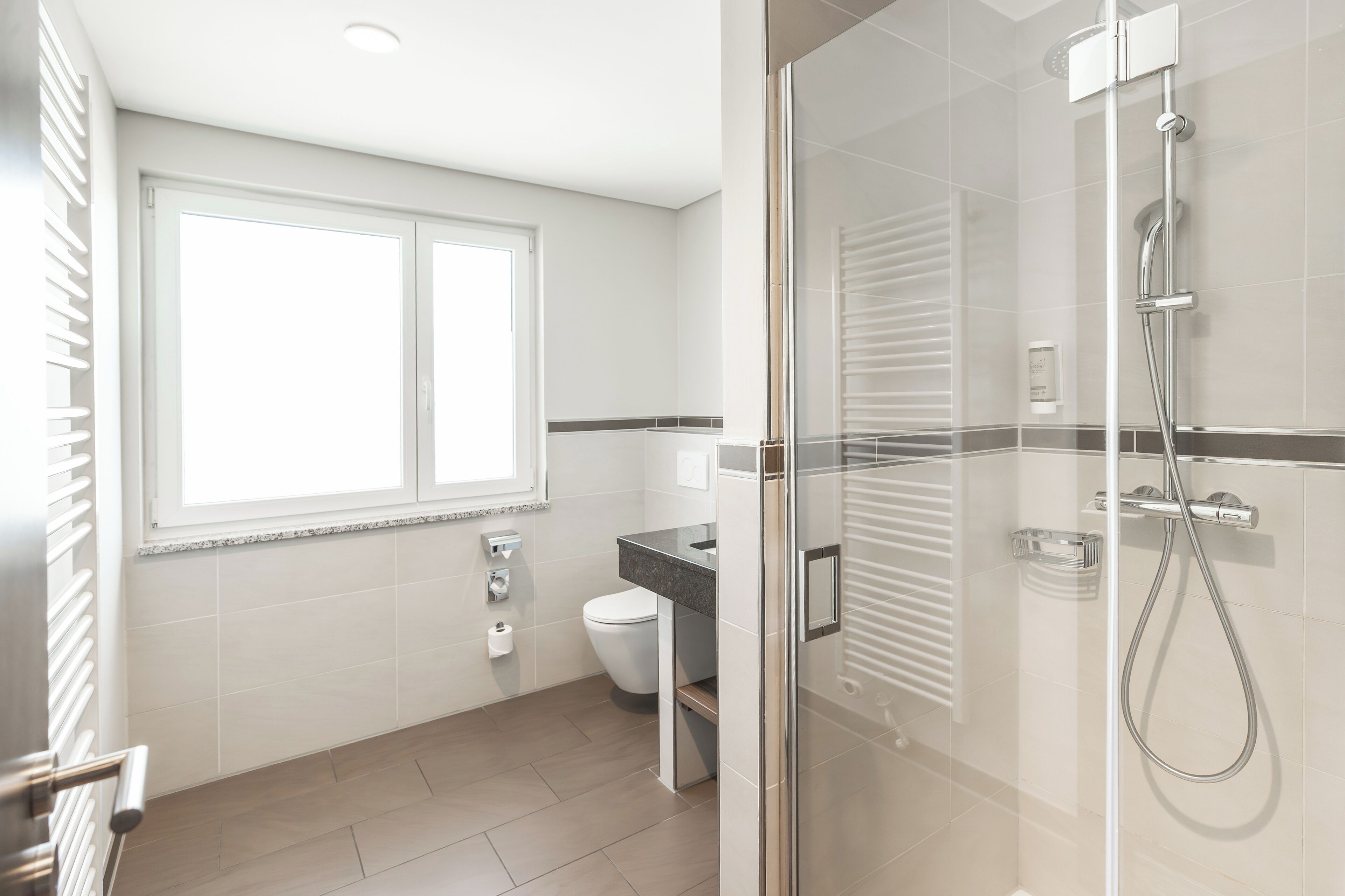 Et moderne badeværelse med brusekabine i glas, toilet og et vindue.