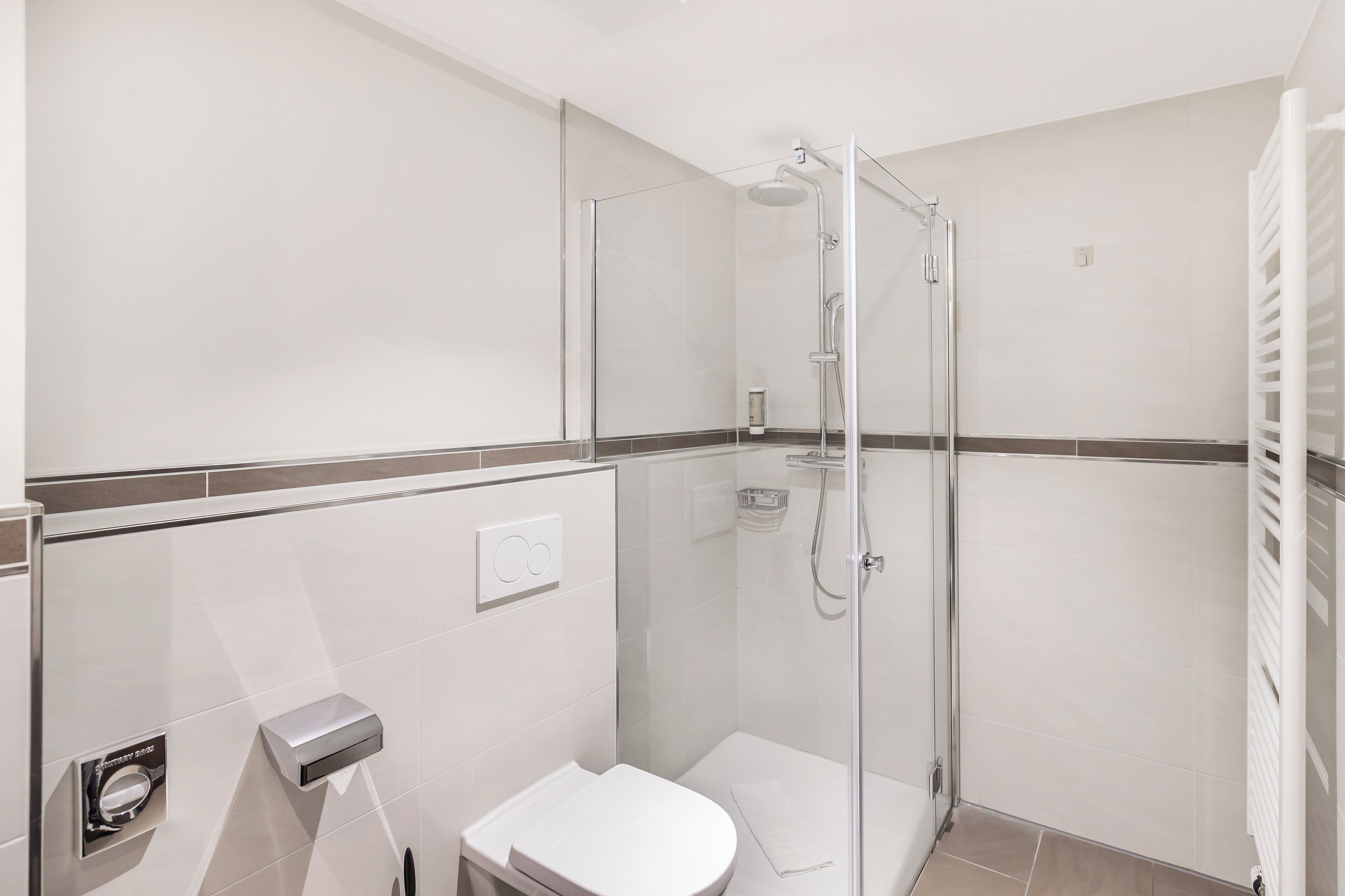 Uma casa de banho moderna com chuveiro de vidro, sanita e um porta-toalhas.