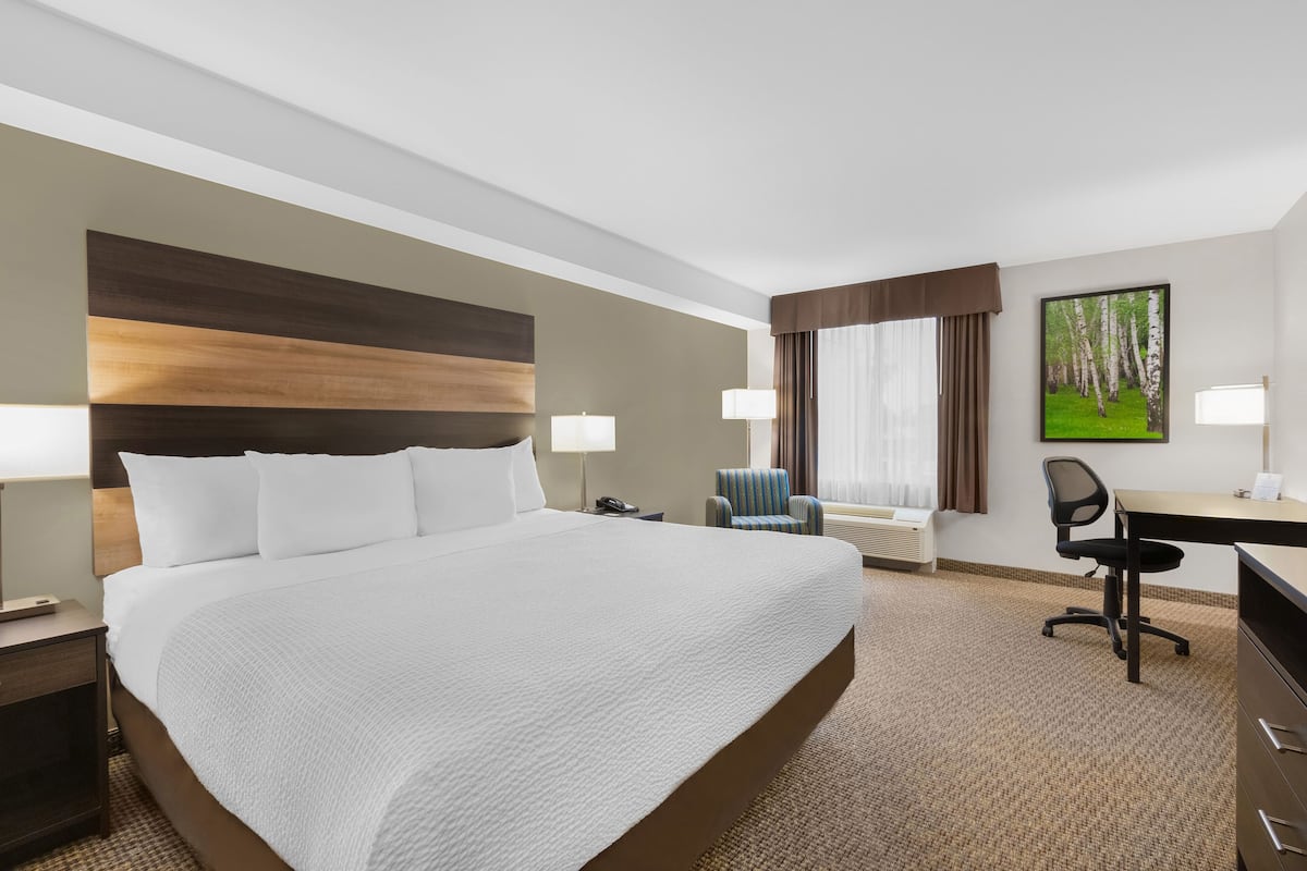 A hotel room with a large bed, a desk, a chair, and a window with curtains.