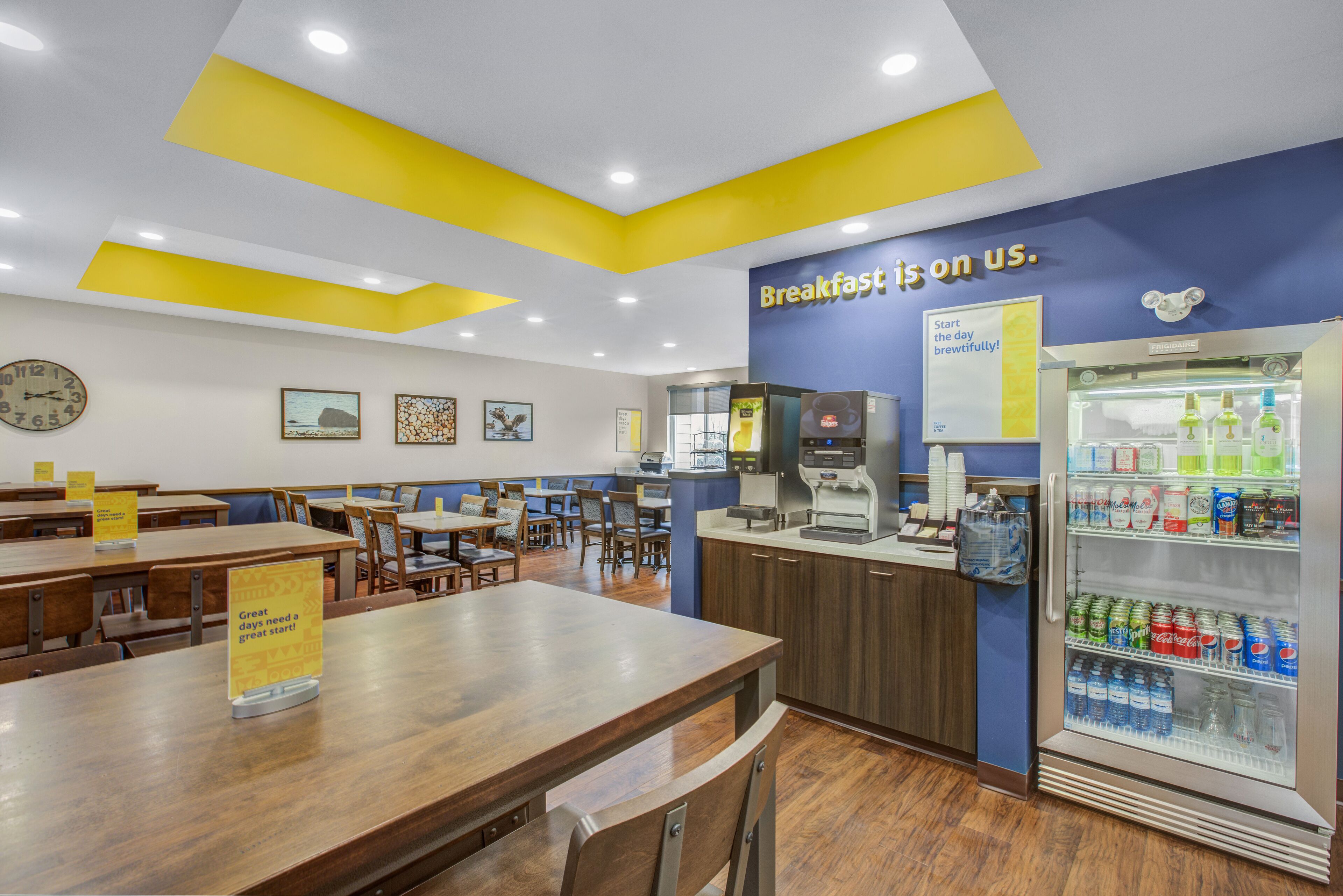 A breakfast area with tables, chairs, a coffee machine, and a refrigerated beverage display.