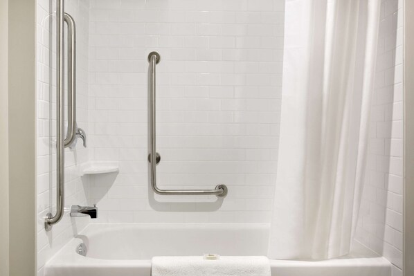 Un baño con una bañera blanca, barras de apoyo y una cortina de ducha.