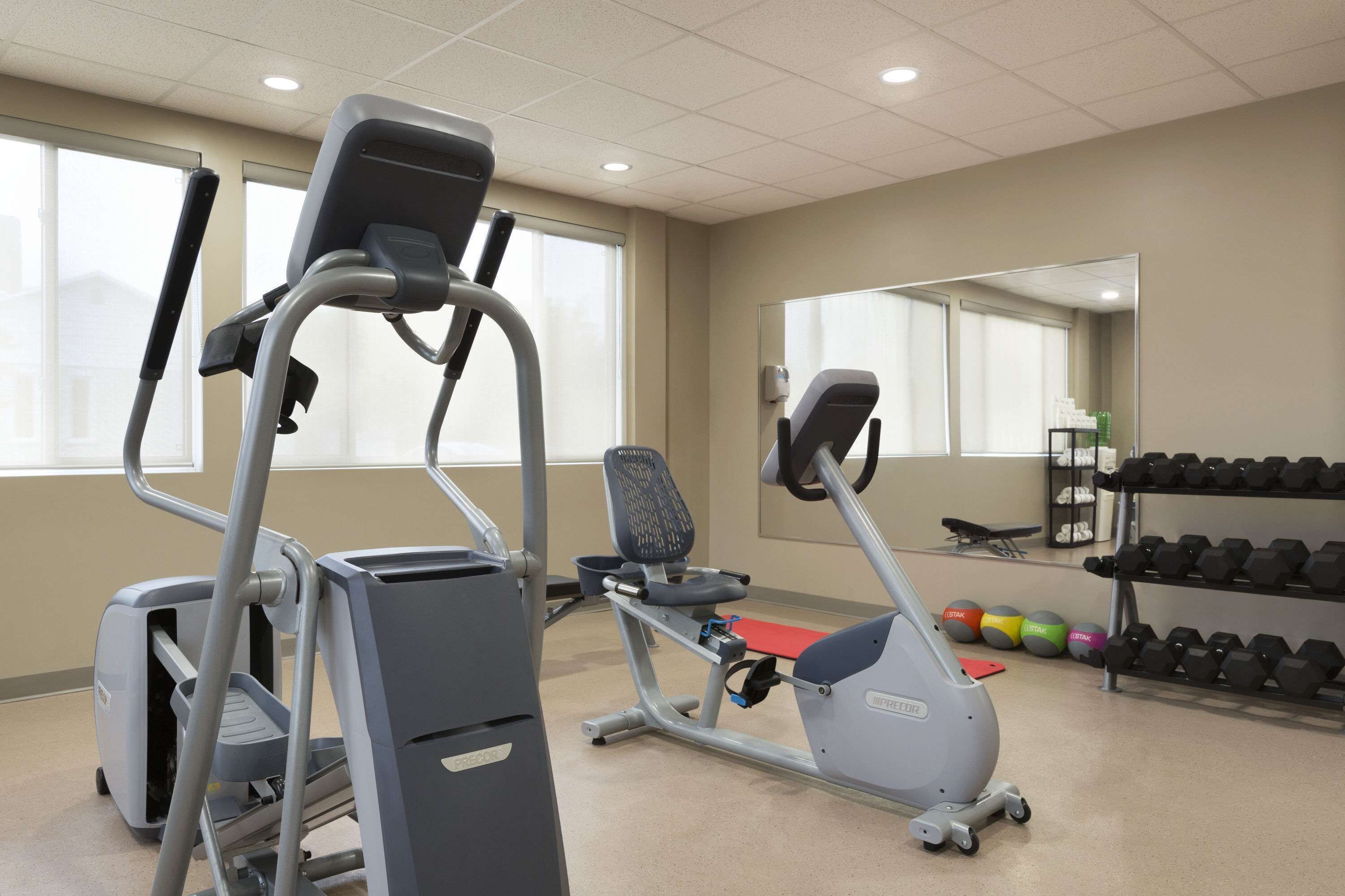Un gimnasio con cintas de correr, elíptica y banco. Hay mancuernas y pelotas de ejercicio.