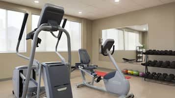Un gimnasio con cintas de correr, elíptica y banco. Hay mancuernas y pelotas de ejercicio.
