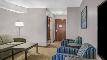 A hotel room with a sofa, a small table, a lamp, and a seating area with patterned chairs.