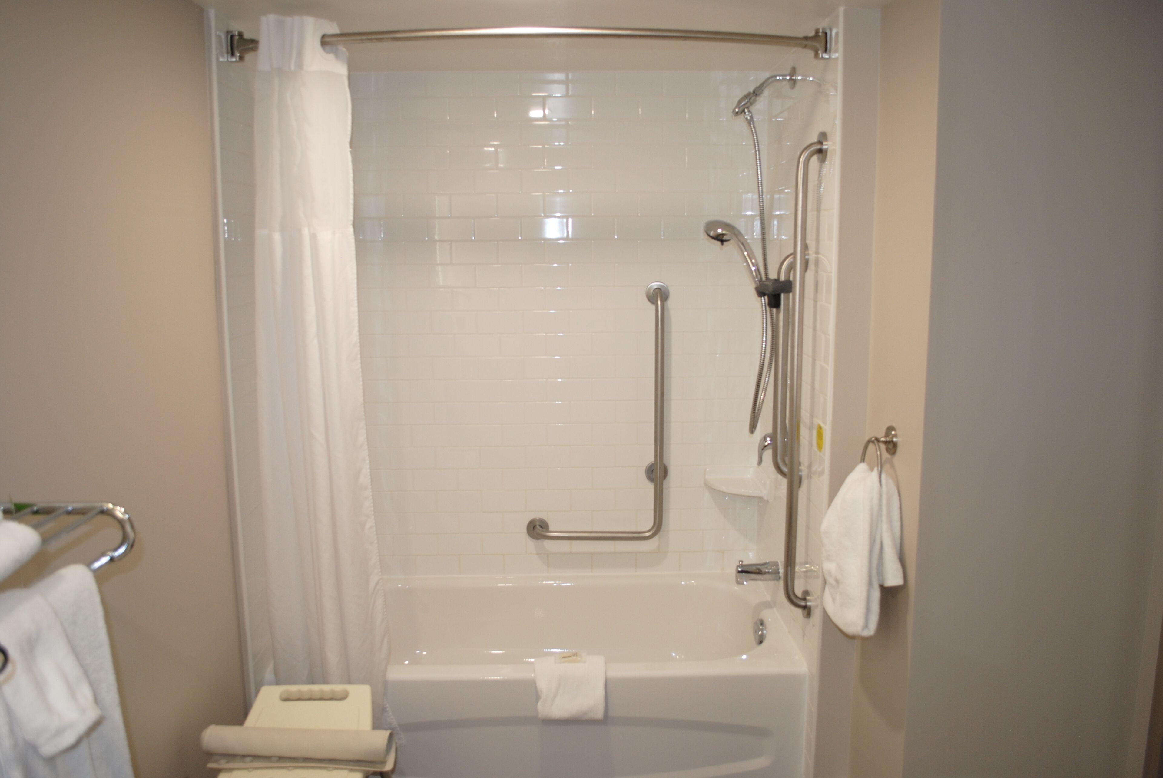 Un baño moderno con cabina de ducha a ras de suelo, barras de apoyo, inodoro con asiento elevado y toallero.