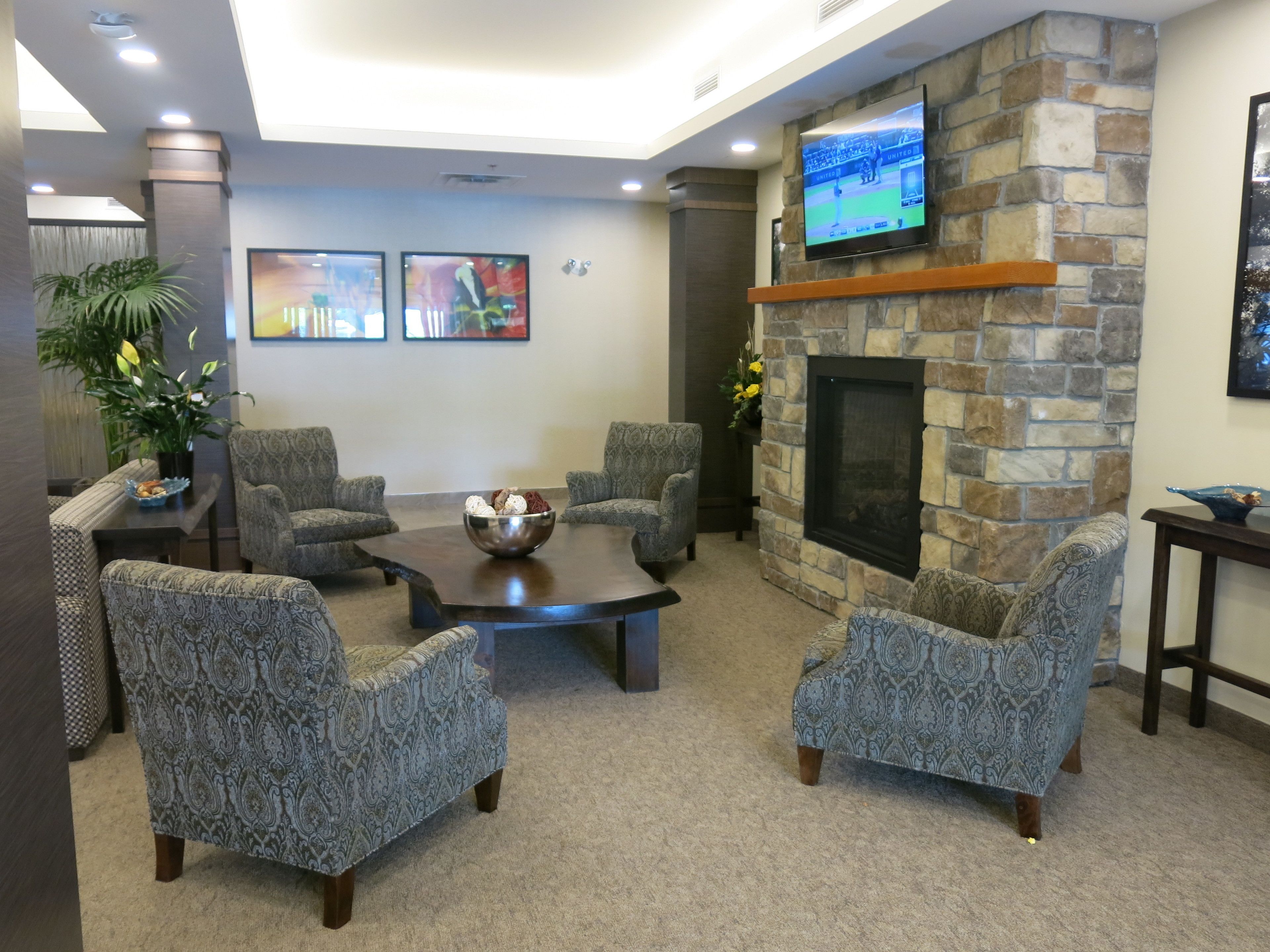 A lobby with four patterned armchairs, a coffee table, a stone fireplace, and a flat-screen TV mounted on the wall.