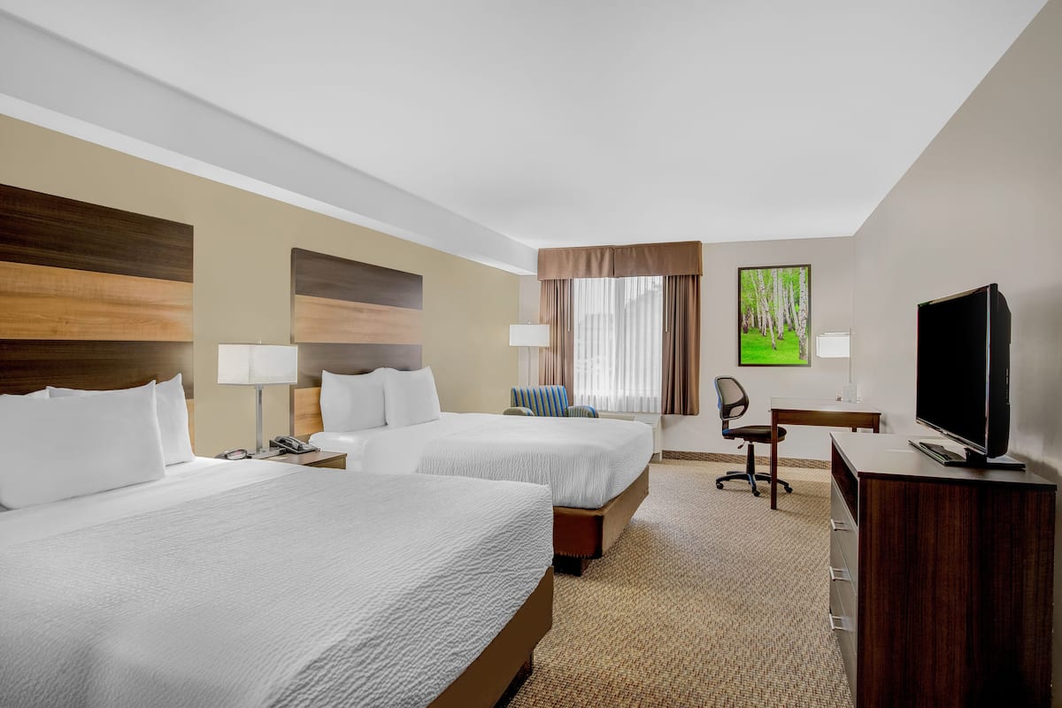 A hotel room with two beds, a desk, a chair, a television, and a painting on the wall.