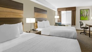 A hotel room with two beds, a desk, a chair, a lamp, and a painting on the wall. - Days Inn & Suites by Wyndham Lindsay (Kawartha Lakes)