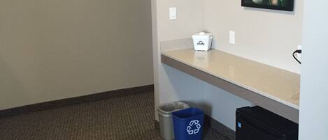 A small, clean room with a beige carpet, a trash bin, a recycling bin, and a picture frame on the wall.
