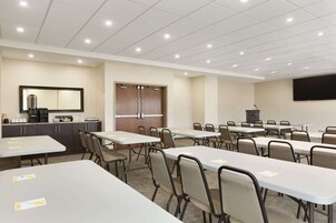 A conference room with multiple tables and chairs, a kitchenette, a large screen, and a door with a mirror.