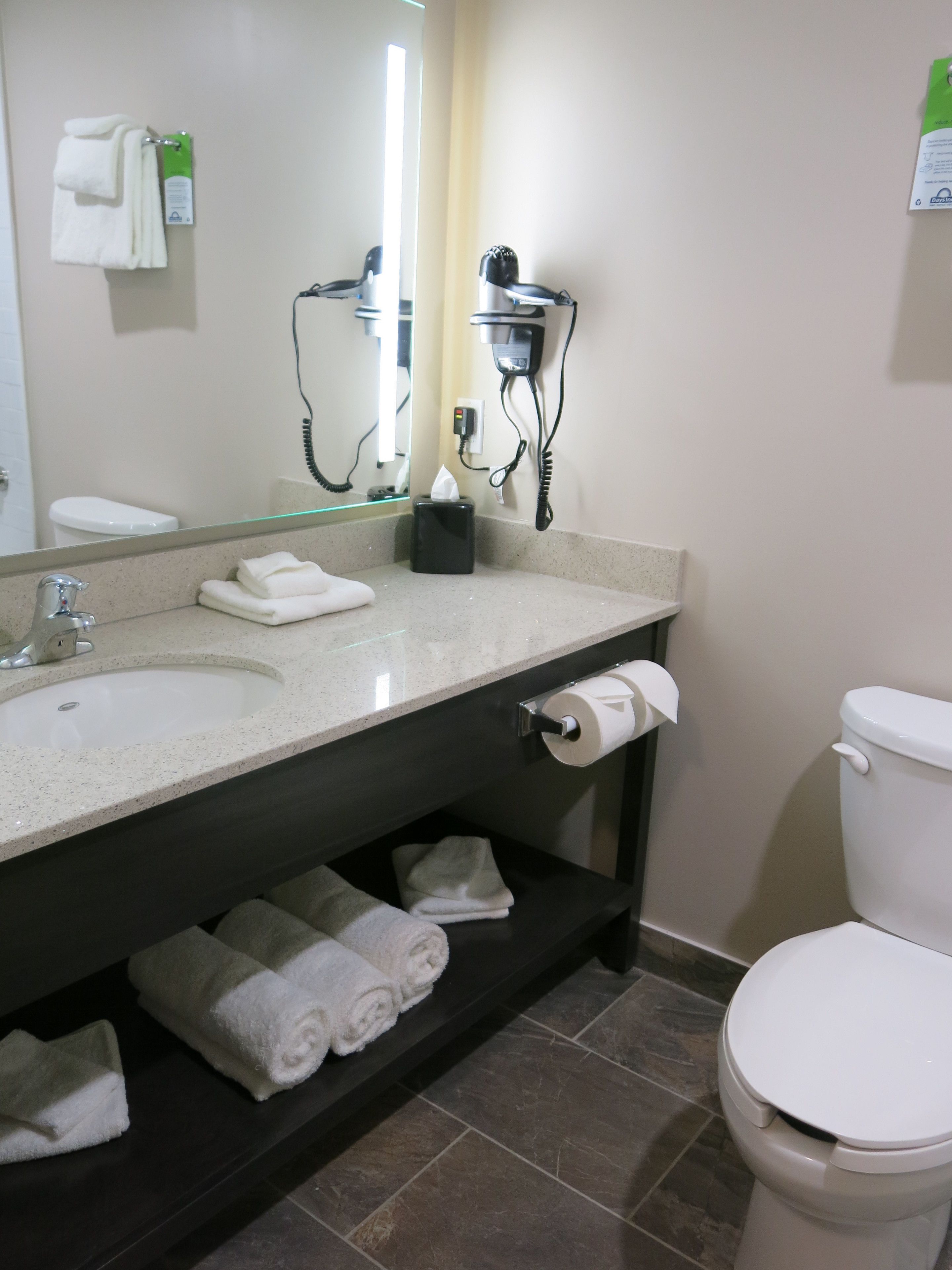 A bathroom with a sink, mirror, towel rack, toilet, and a shelf with towels.