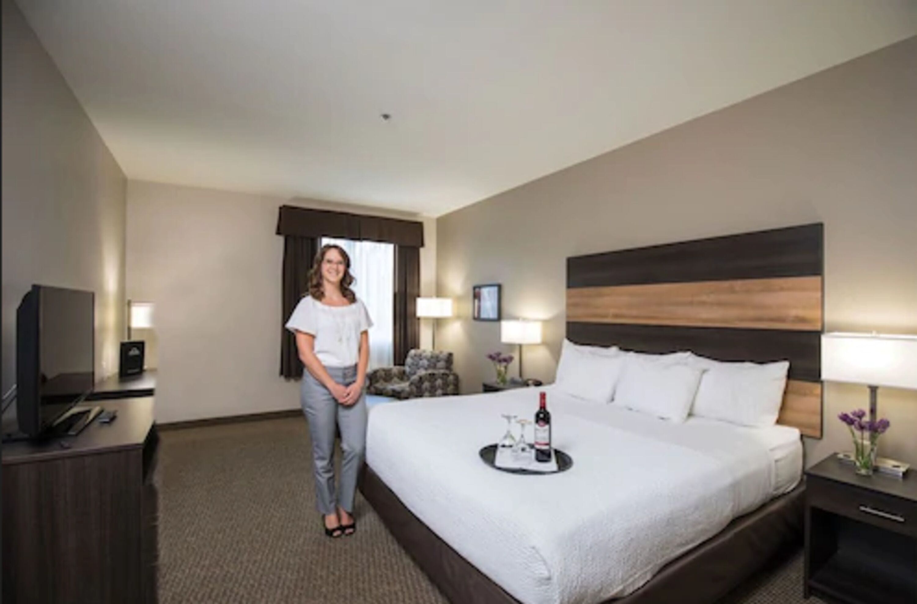 A hotel room with a large bed, a TV, a desk, and a window with curtains.