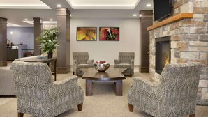 A modern living room with a stone fireplace, a round coffee table, and patterned armchairs. - Days Inn & Suites by Wyndham Lindsay (Kawartha Lakes)