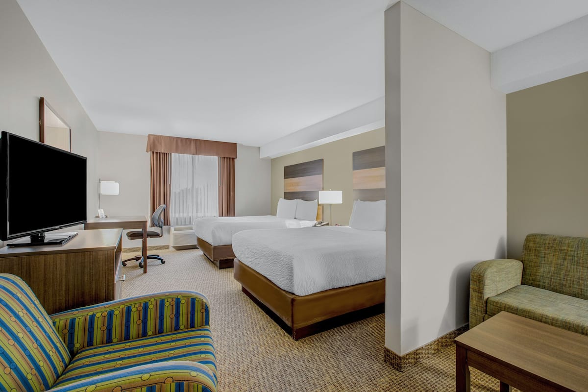 A hotel room with a television, two beds, a desk, a chair, and a sofa.