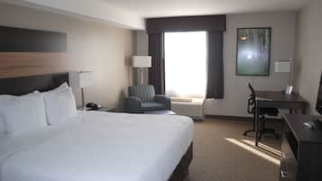Une chambre d’hôtel avec un grand lit, un bureau, une chaise et une fenêtre avec des rideaux.