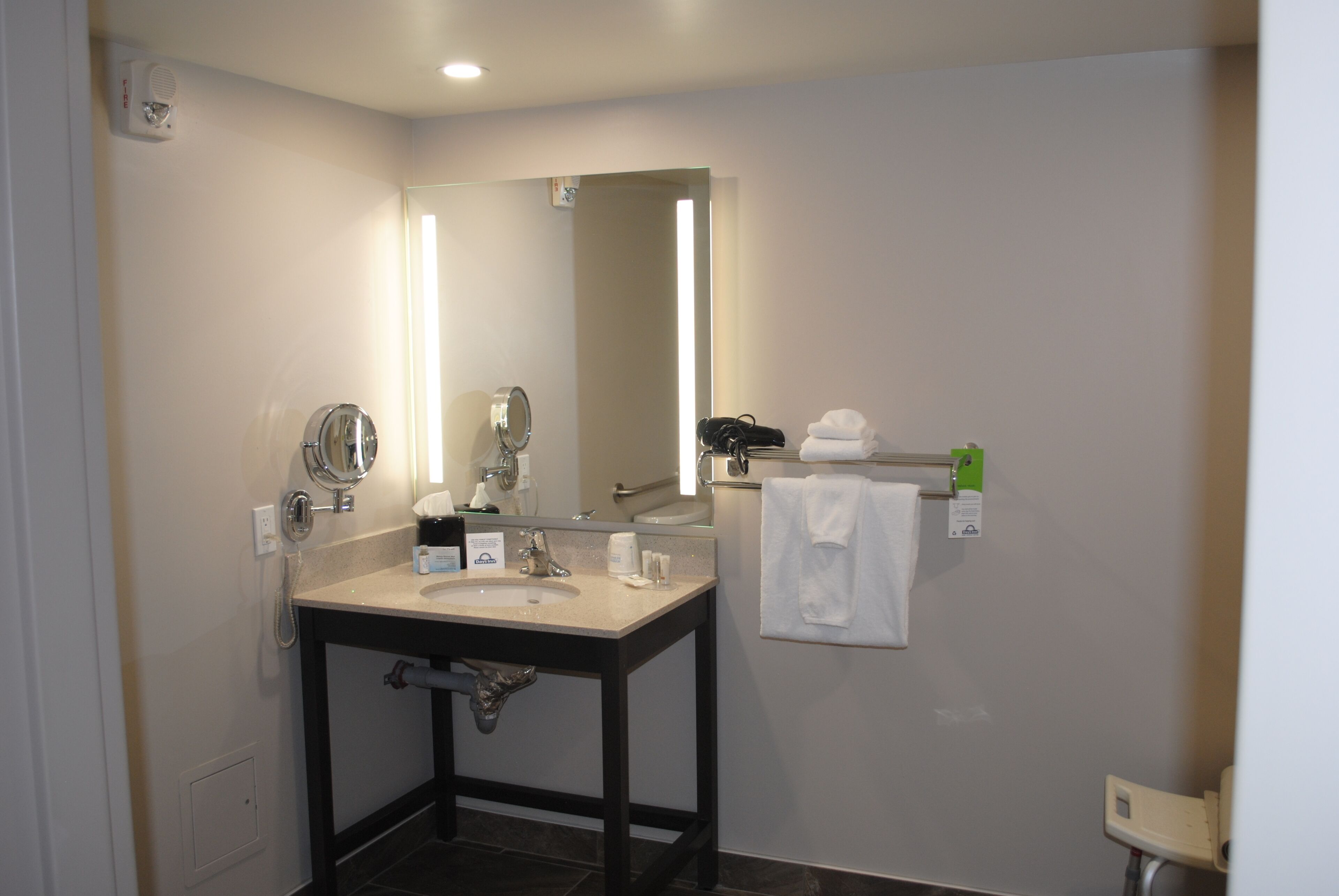 Un baño moderno con lavamanos, espejo, toallero y cabezal de ducha de mano.