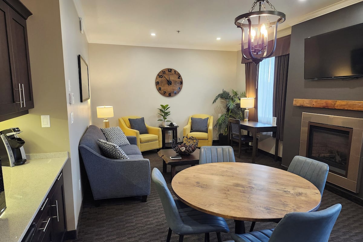 A modern living room with a round wooden table, two sofas, a coffee machine, a clock, and a fireplace.