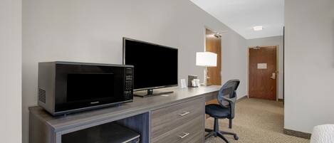 A hotel room with a kitchenette, a flat-screen TV, a desk, a chair, and a door leading to another room.