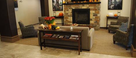 Una sala de estar con chimenea, dos sillones, una mesa de centro con revistas y un televisor montado en la pared.