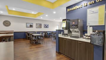 A breakfast area with tables, chairs, a coffee machine, and a clock on the wall.