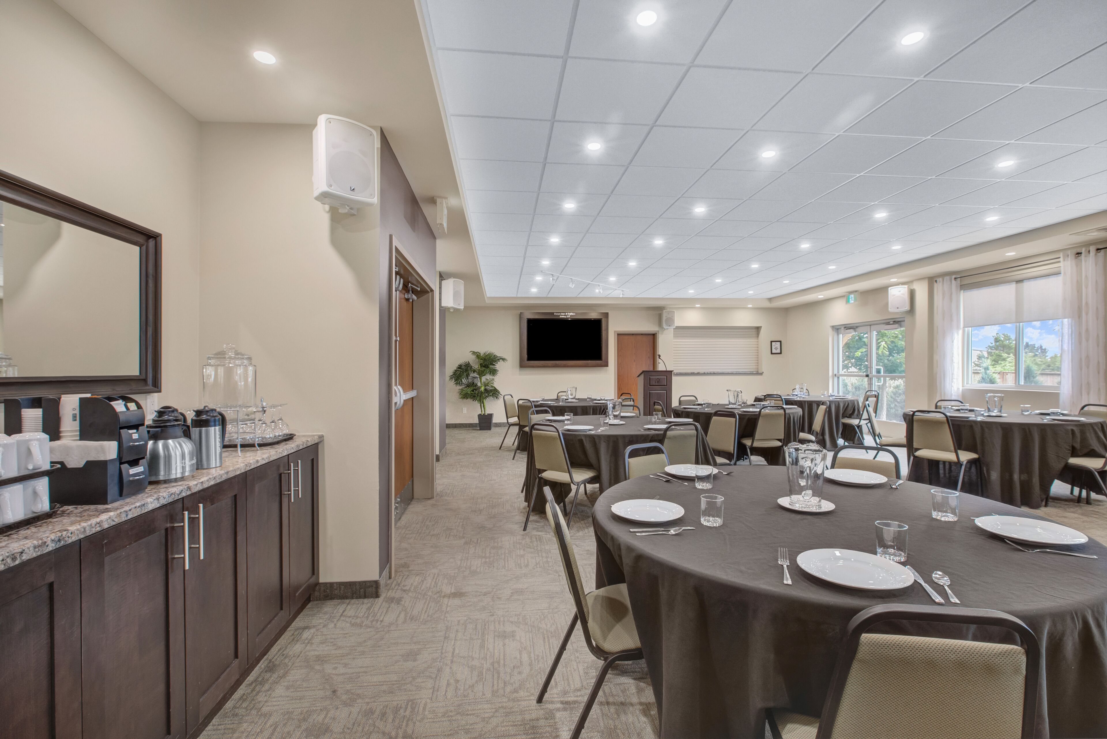 A conference room with round tables, chairs, and a buffet area with coffee makers and a TV.