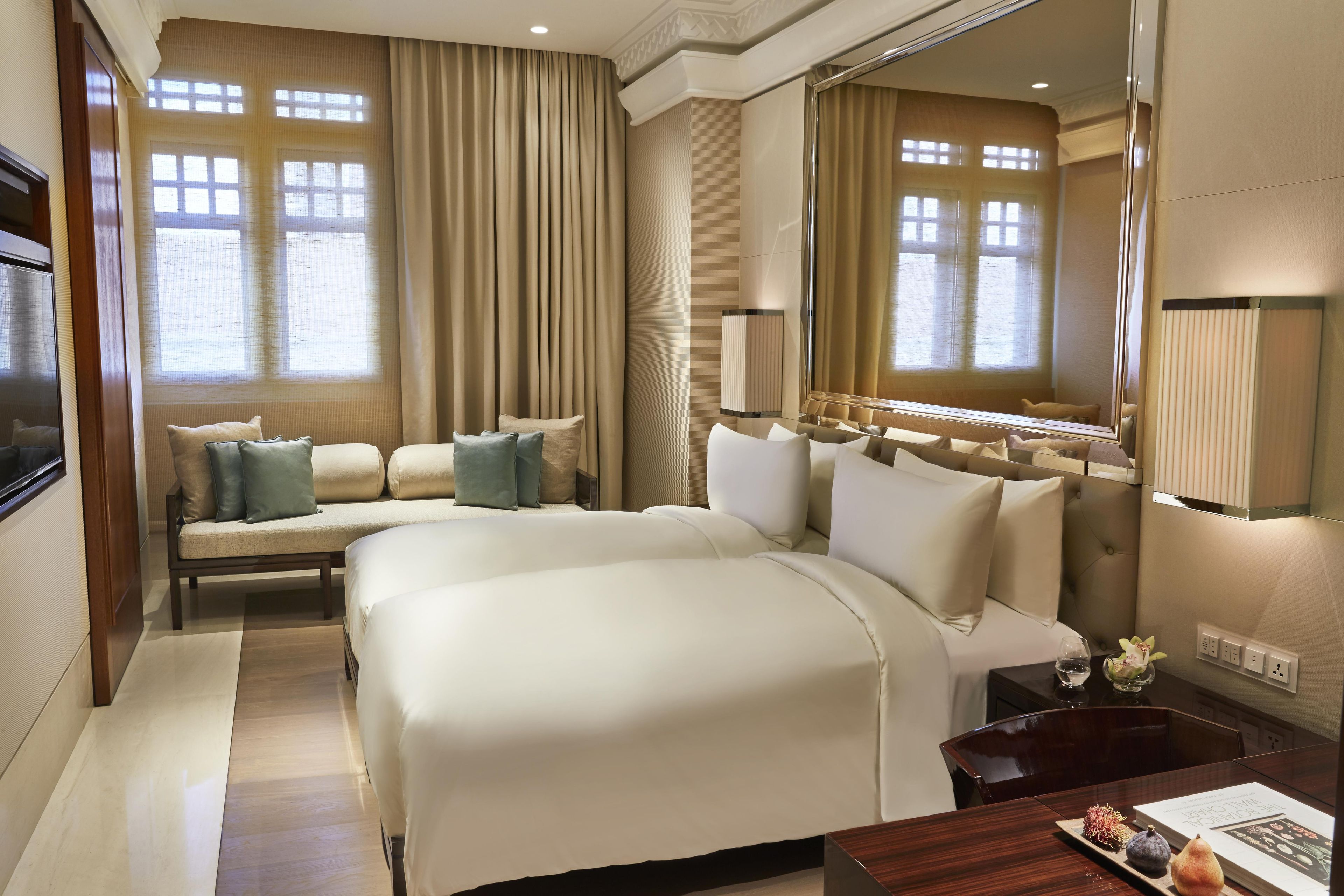 A hotel room with a large bed, a sofa, a desk with a lamp, and a large mirror.