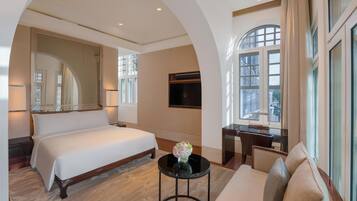 Habitación de hotel con una cama grande, un escritorio, una silla, un televisor y vistas a la ciudad desde las ventanas.