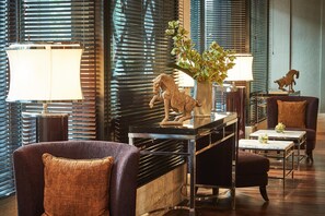 Eine moderne Hotellobby mit Sitzgelegenheit, inklusive Sofa und Sesseln, einer dekorativen Pferdeskulptur, einer Blumenvase und einer Lampe.