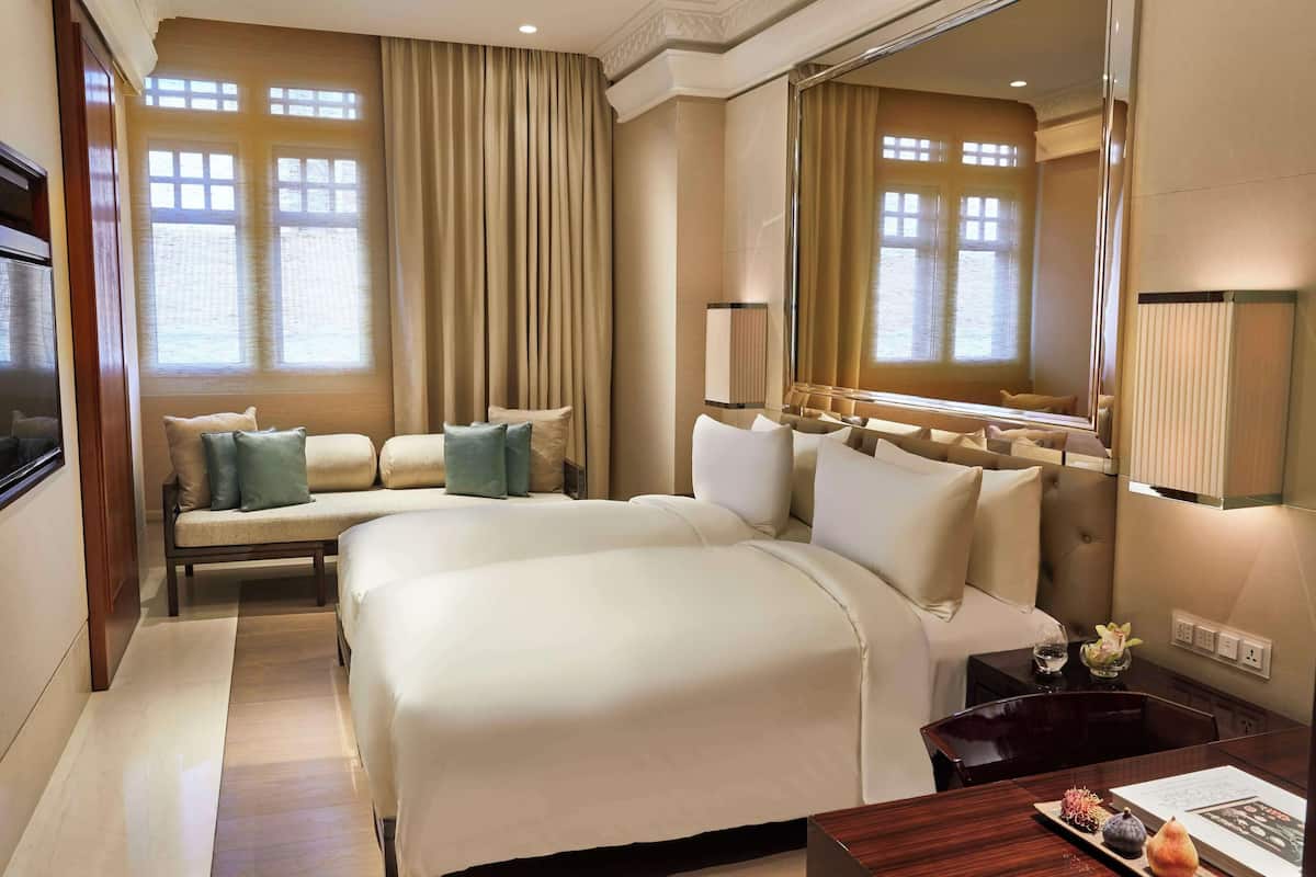 A hotel room with a large bed, a sofa, a desk with a lamp, and a large mirror.