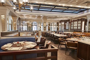 L’intérieur d’un restaurant se caractérise par de hauts plafonds, des lustres et une vue sur la rue grâce à de grandes fenêtres.