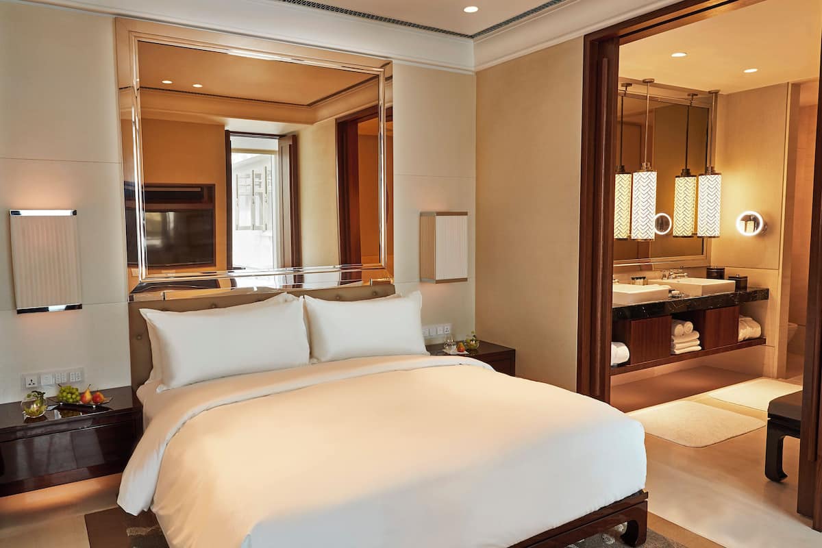 A hotel room with a large bed, a bathroom with a vanity and mirror, and a view of the hallway.