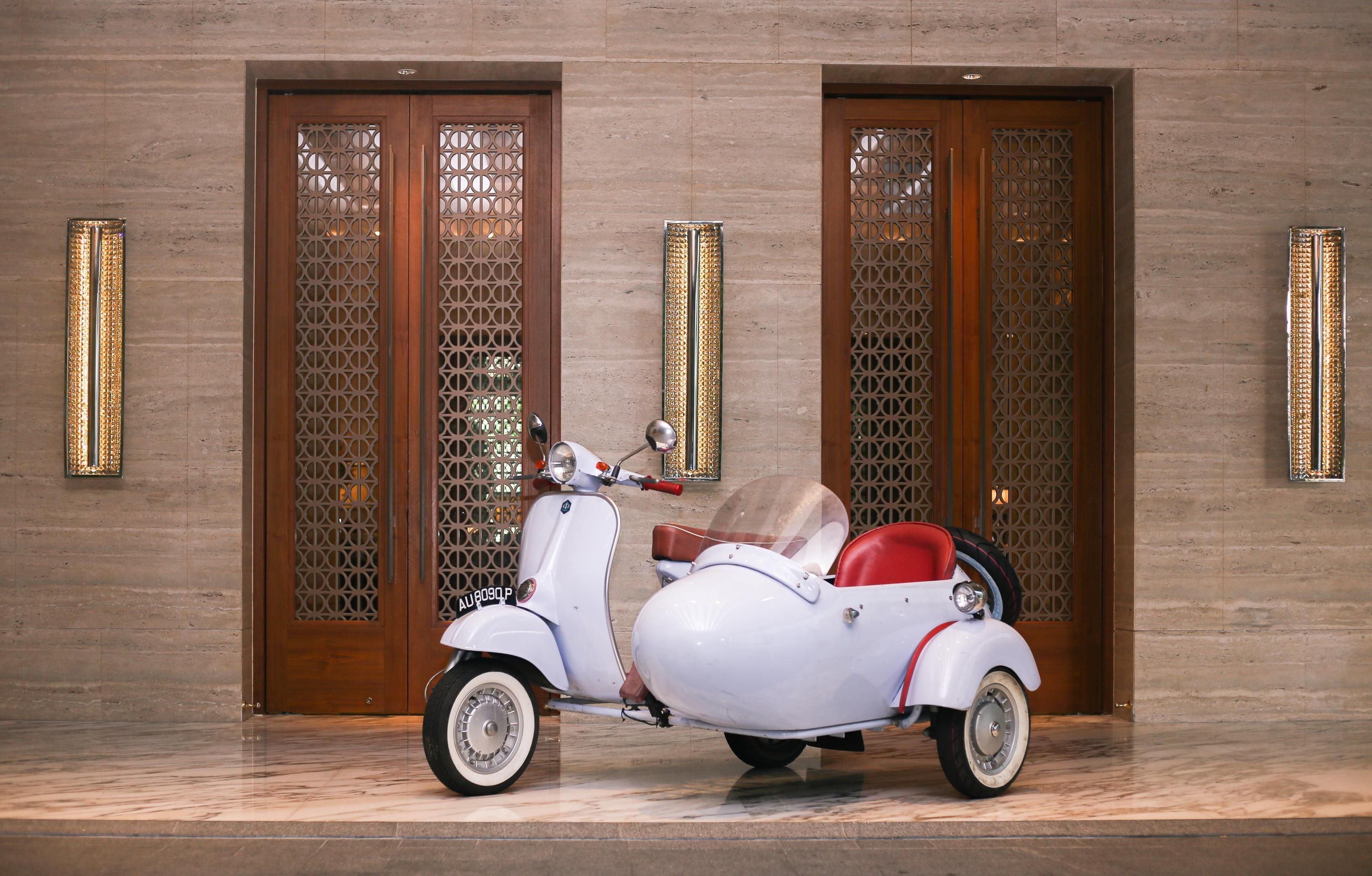 A white scooter with a sidecar parked in front of a building with wooden doors and decorative panels.