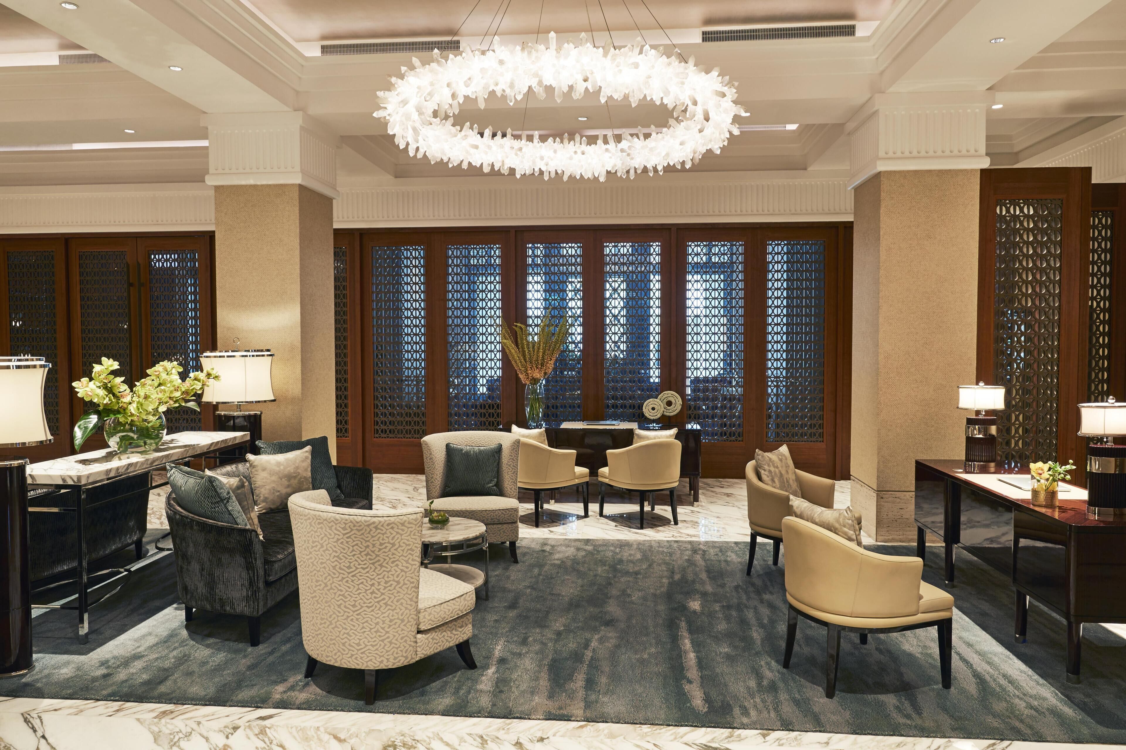 A hotel lobby with a chandelier, seating area, and decorative screens.