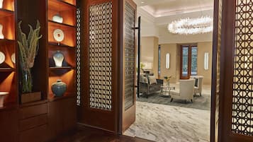 A hotel lobby with a wooden reception desk, a seating area with armchairs, and a decorative screen with a geometric pattern.