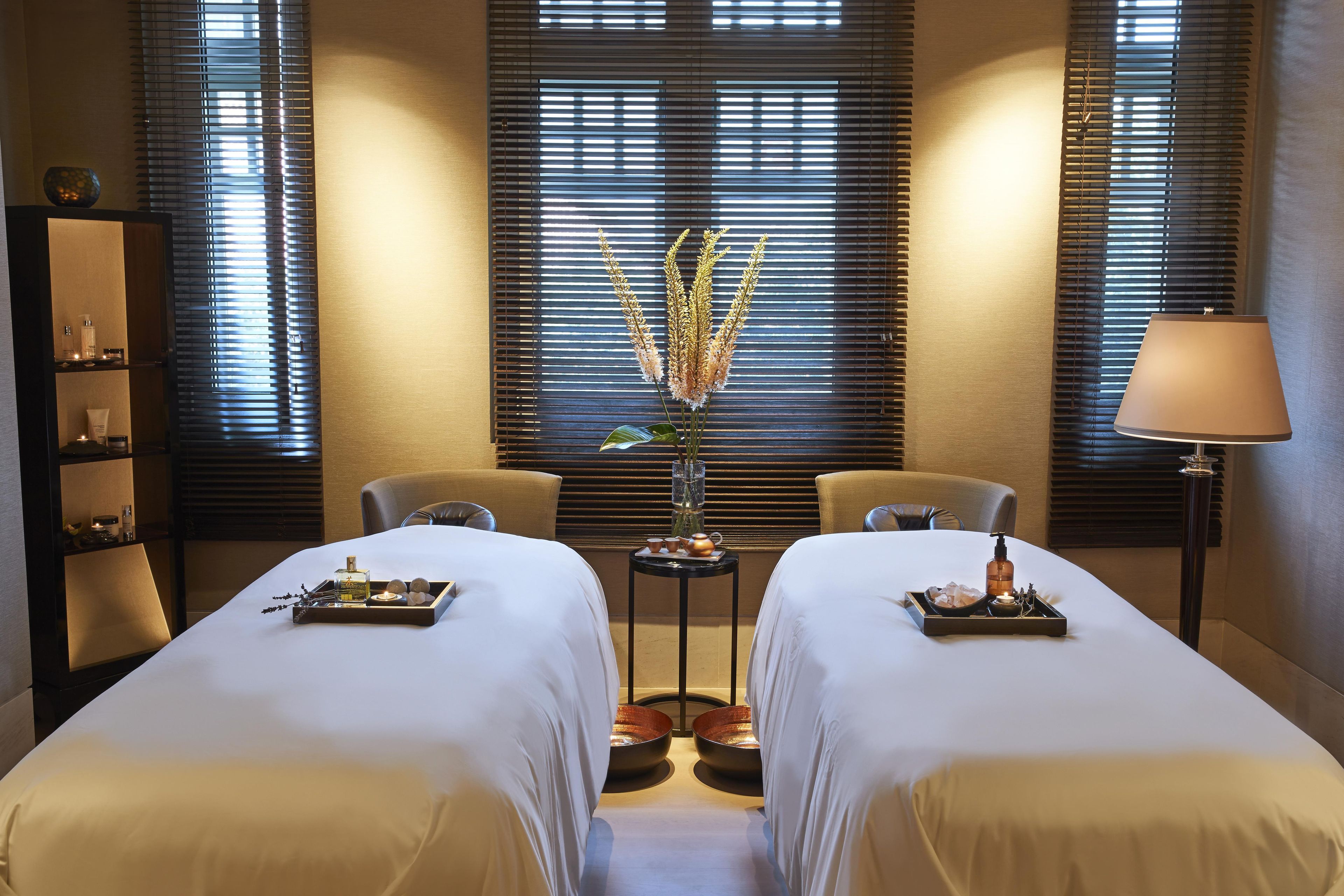 A hotel room with two beds, a small table with a vase of flowers, and a lamp.