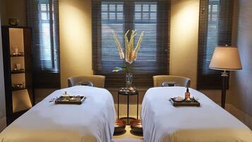 A hotel room with two beds, a small table with a vase of flowers, and a lamp.