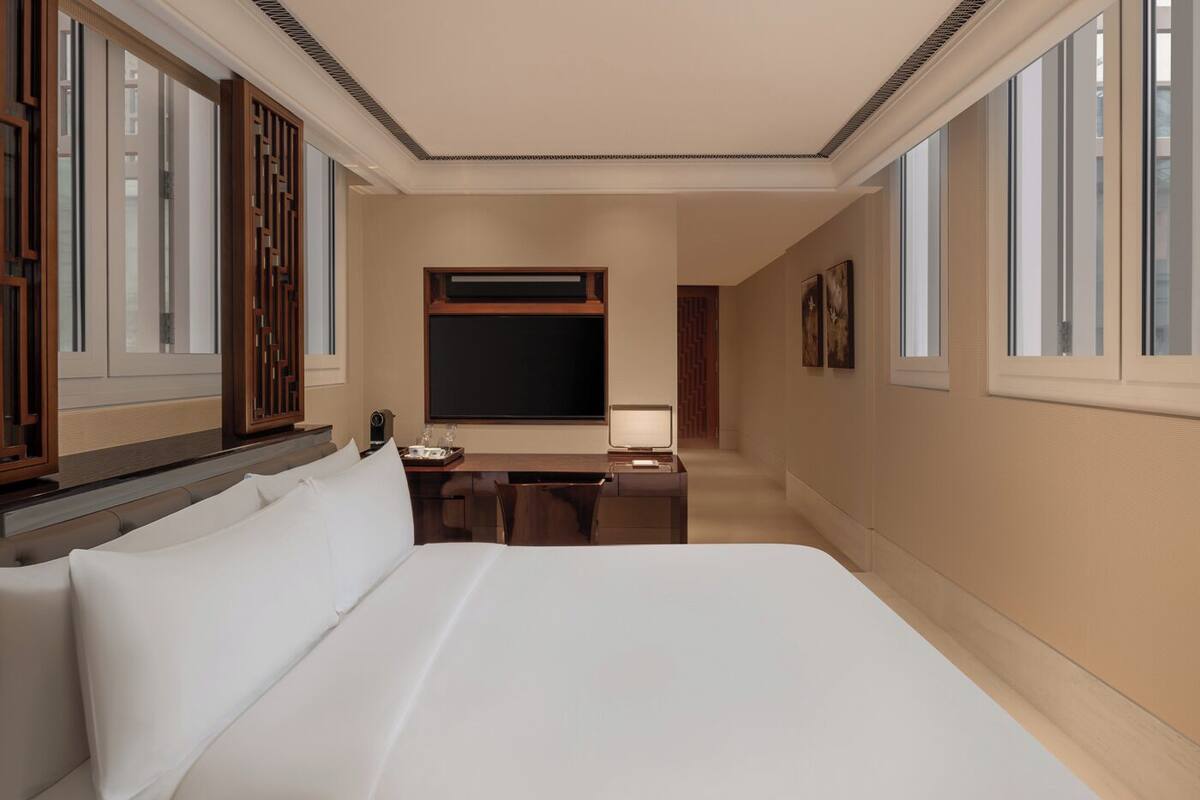 A hotel room with a large bed, a desk with a chair, a TV, and a window with wooden shutters.