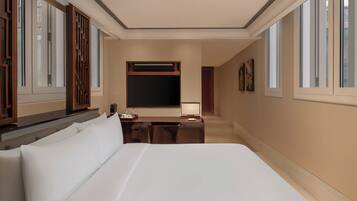 A hotel room with a large bed, a desk with a chair, a TV, and a window with wooden shutters.