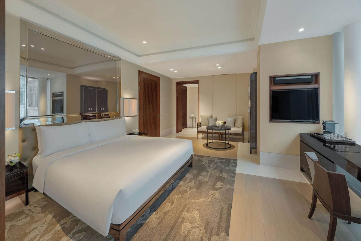 A hotel room with a large bed, a desk with a chair, a television, and a mirror.