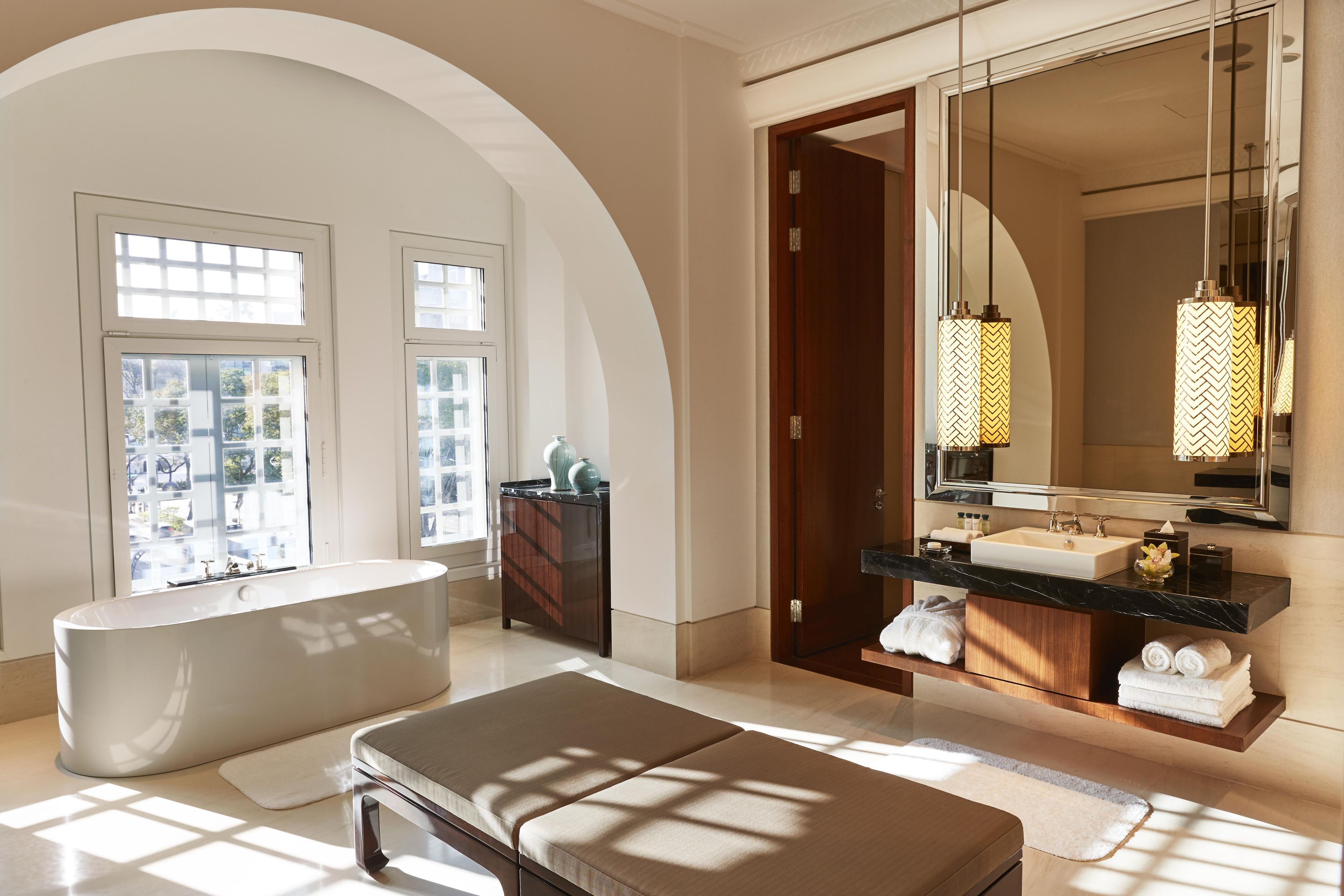 Ein modernes Badezimmer mit einer freistehenden Badewanne, einem Waschtisch mit großem Spiegel und einer Tür zu einem anderen Raum.