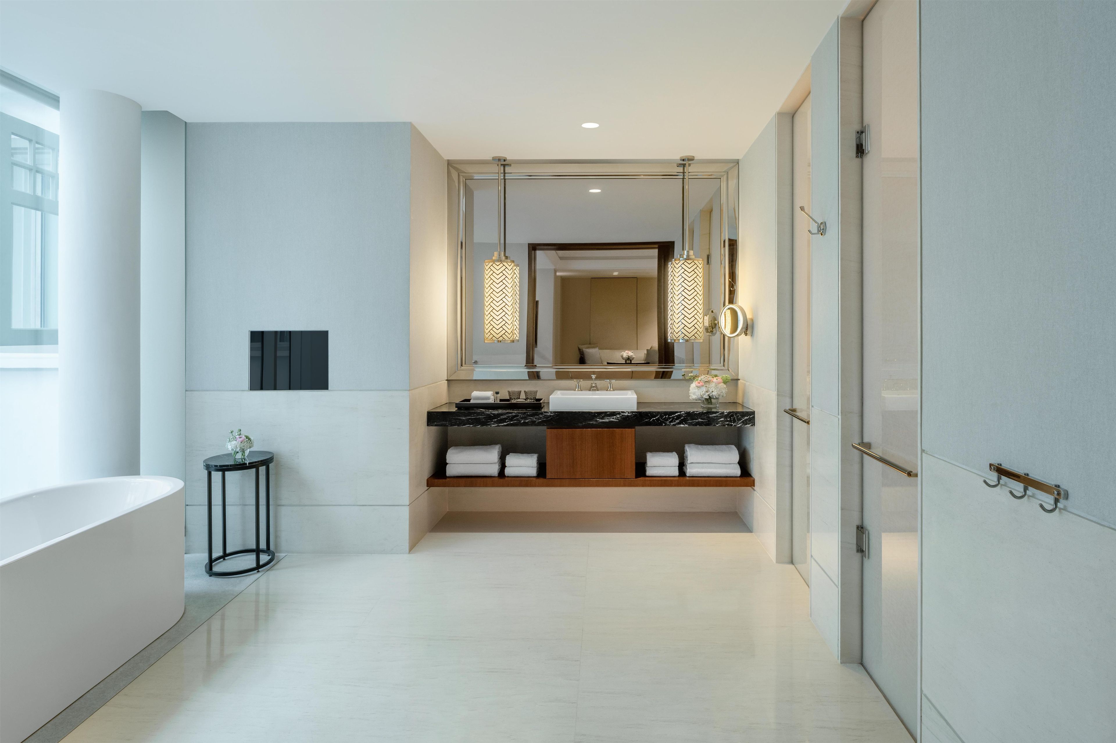 Une salle de bain moderne avec un grand miroir, une baignoire et un meuble-lavabo doté d’un plan de travail en marbre.