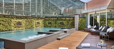 A rooftop pool area with lounge chairs and a glass-enclosed building in the background.