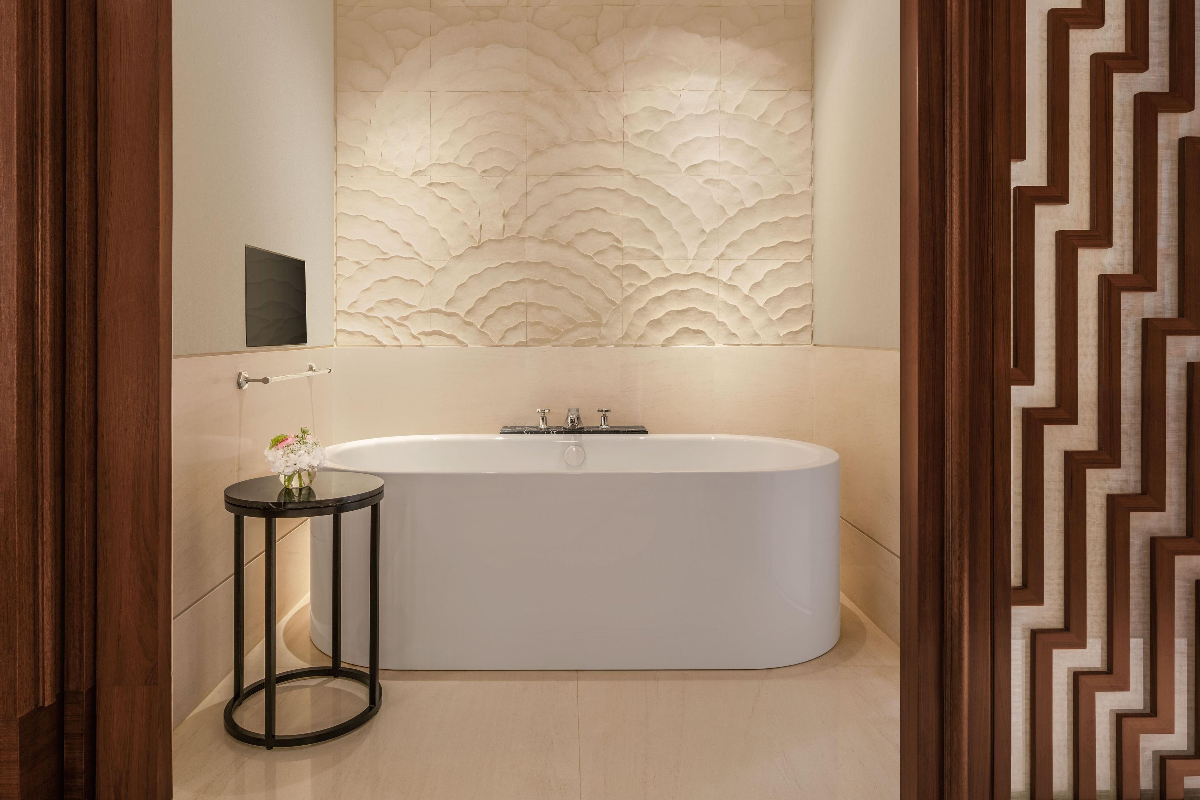 A modern bathroom with a freestanding bathtub, a small round table with a vase, and a decorative wall panel.