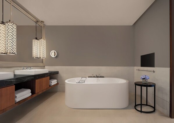Un baño moderno con una bañera independiente, un espejo grande y lámparas colgantes.