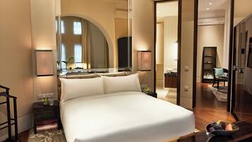 Ein Hotelzimmer mit einem großen Bett, einem Nachttisch mit Lampe, einem Spiegel sowie Blick ins Bad und den Essbereich.