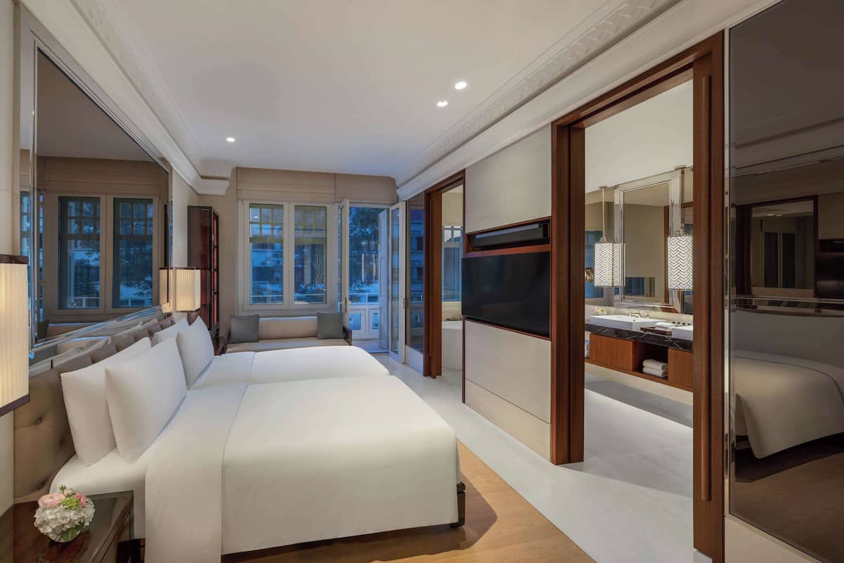 A spacious bedroom with a large bed, a TV, and a bathroom with a vanity and mirror.